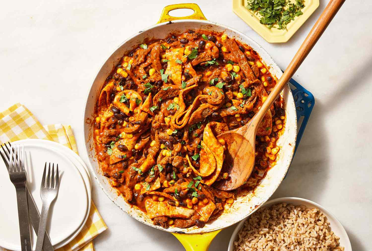 carne asada burrito skillet with a stack of plates, and bowl of brown rice nearby.