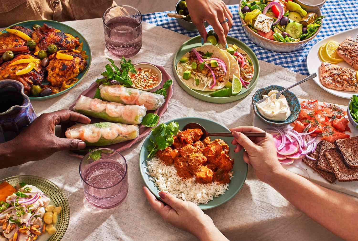 An array of foods from around the world on a tabletop with hands reaching in