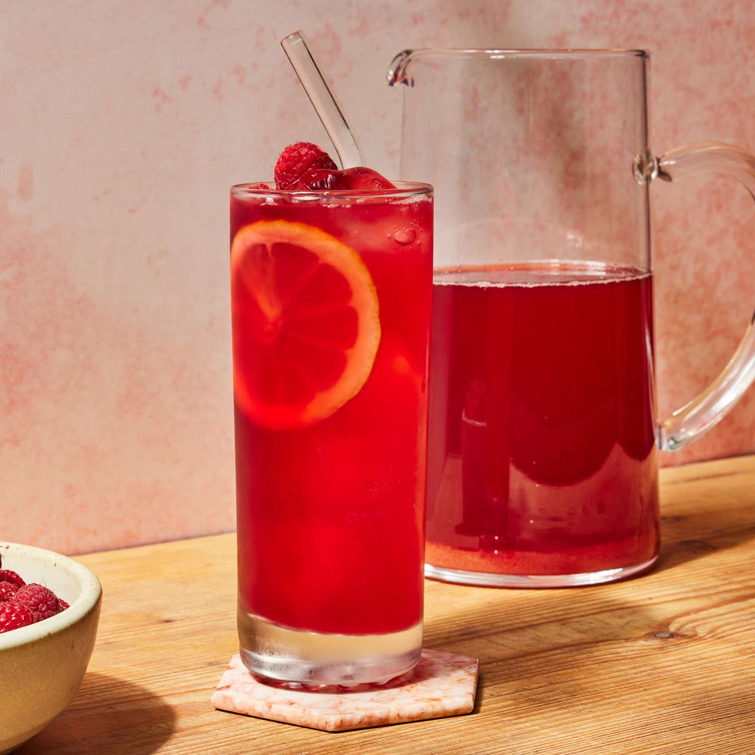 a recipe photo of the Raspberry Iced Tea poured in a glass and a pitcher full of the Raspberry Iced Tea